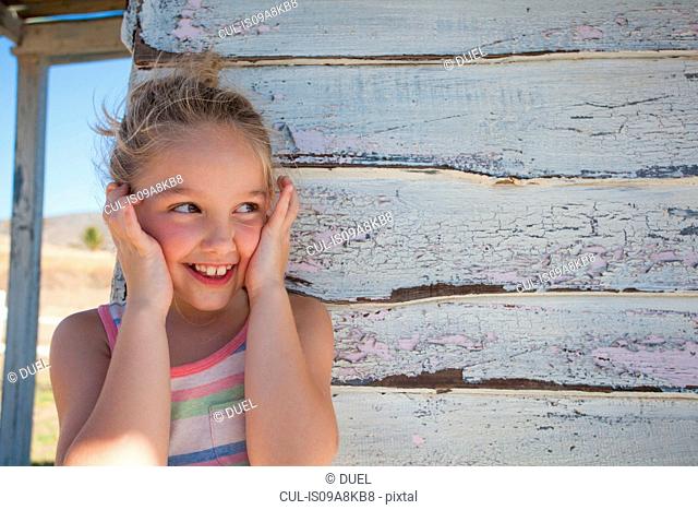 Portrait of girl with finger in ears by clapboard cabin