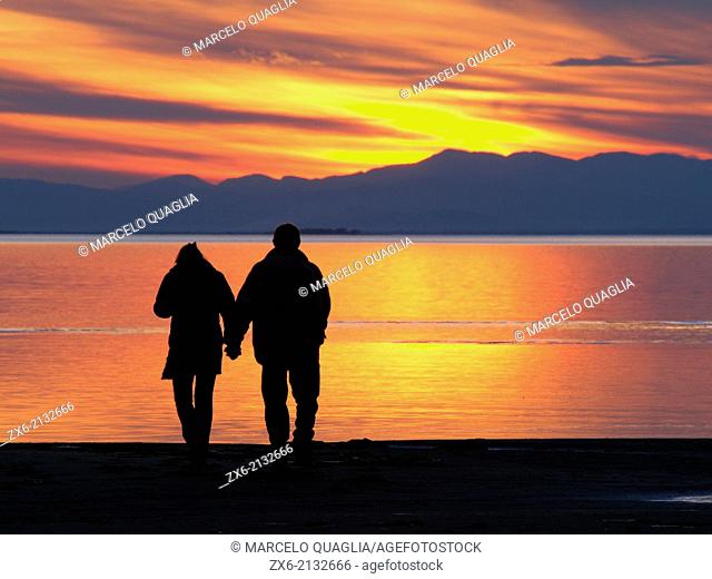 Couple walking towards sunset at Alfacs Bay. Ebro River Delta Natural Park, Tarragona province, Catalonia, Spain