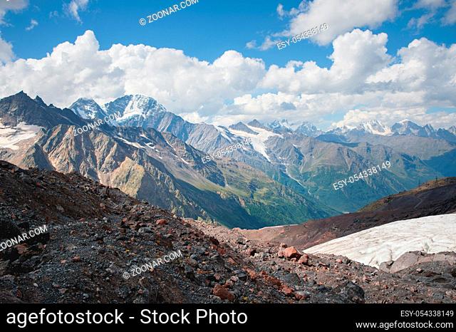 Mountain landscape dusty dirty volcanic slope with a cracked melting glacier against the backdrop of the Caucasus Mountains. Global warming