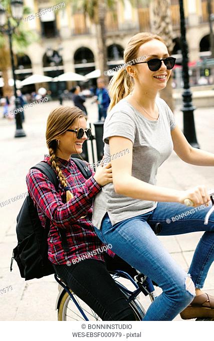 Spain, Barcelona, two happy young women sharing bicycle in the city