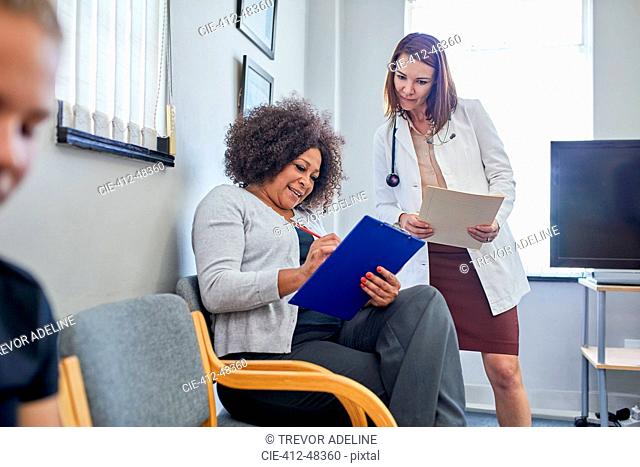 Female doctor and patient discussing paperwork in clinic waiting room