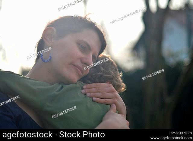 Happy mother holding little child in her arms with love in a garden outdoors in summertime
