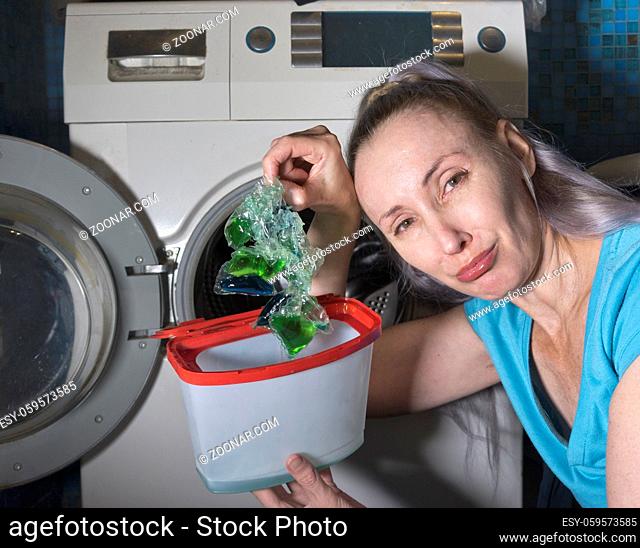 woman in the bathroom, next to the washing machine, takes out the defective washing gel stuck into one lump from the packaging and crying, photo from the series