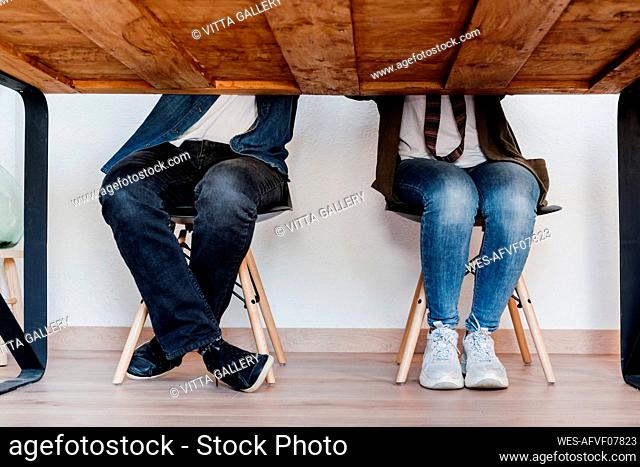 Male and female colleagues in casuals sitting on stool at home office