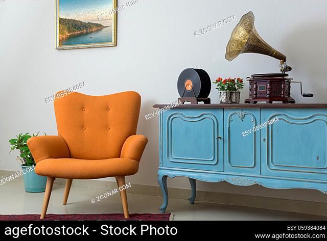 Interior of retro orange armchair, vintage wooden light blue sideboard, old phonograph (gramophone), vinyl records on background of beige wall