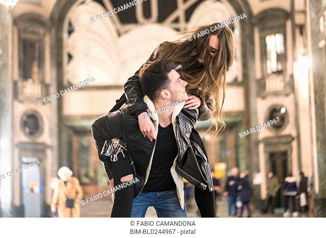 Caucasian man carrying woman piggyback in lobby