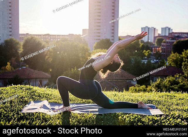Young woman practicing yoga in warrior position at city park during sunny day