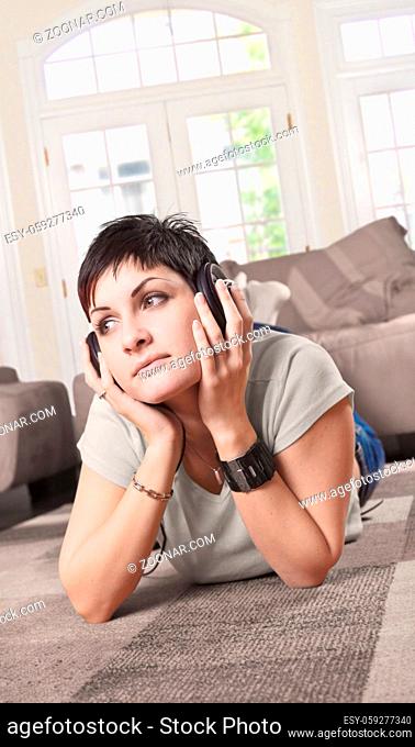 Women is lying on the floor in the living room and listening music on headphones