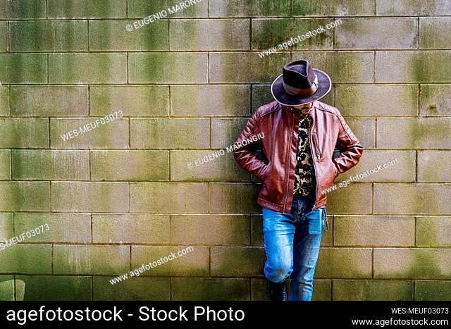 Man wearing leather jacket leaning on wall