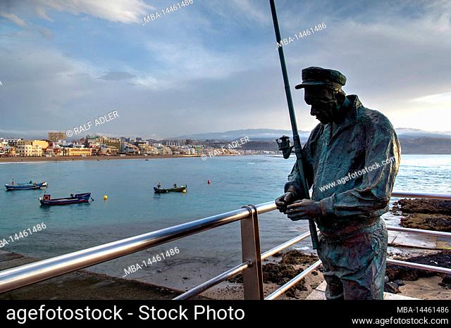 Spain, Canary Islands, Gran Canaria, Las Palmas, Playa de las Canteras, bronze statue of an angler, sky cloudy, boats in the water, houses in the background