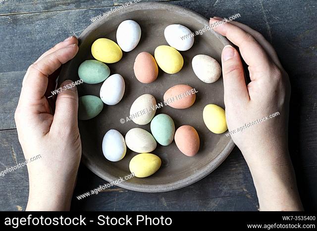 Hands holding stylish pastel painted easter eggs in ceramic grey plate on vintage old wooden background, Happy Easter concept
