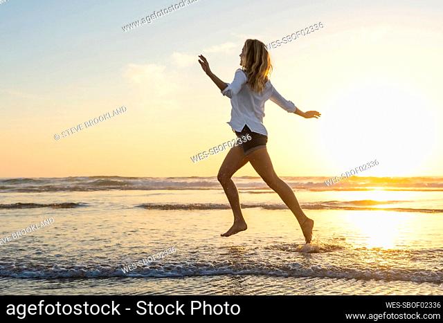 Carefree woman running with arms outstretched against sea during sunset