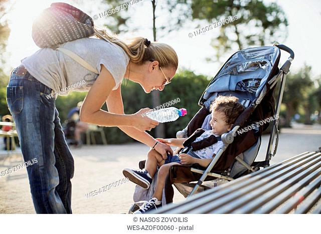Mother giving water bottle to his son, sitting in pram
