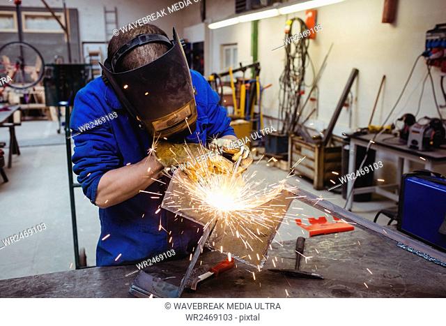 Welder cutting metal with grinder with workshop