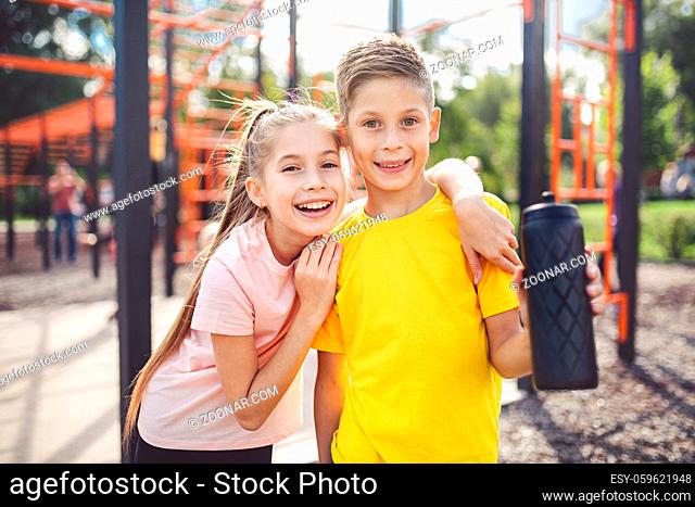 Teens children and sports theme. Two kids athletes twins rest and replenish their thirst during workout outdoor gym workout in sunny summer weather