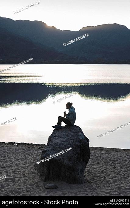 Man sitting on rock at lake during sunset