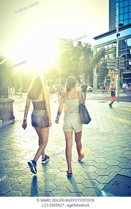 Two young women walking down the street at sunset. Barcelona, Catalonia, Spain