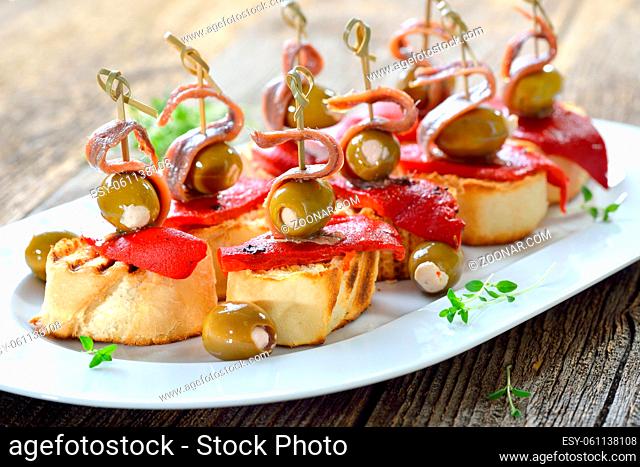 Spanische Tapas: Gegrilltes Baguette mit geroestetem und eingelegtem Paprika, gefuellten Oliven und Sardellenfilets - Spanish snack: Grilled bread with roasted...