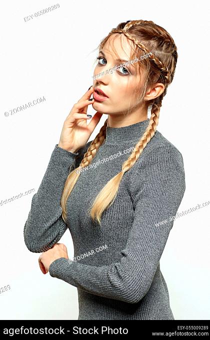 Portrait of beautiful young dark blonde woman. Female with creative braid hairdo on gray background. Girl with hand near face