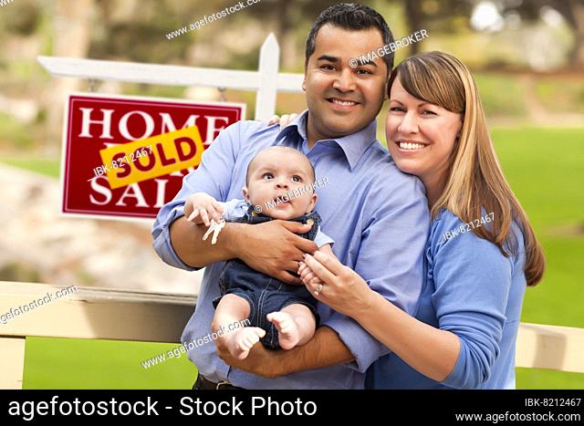 Happy mixed-race couple with baby in front of sold real estate sign