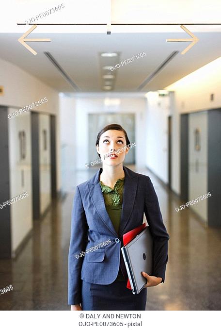 Businesswoman in corridor looking up at arrows pointing opposite directions