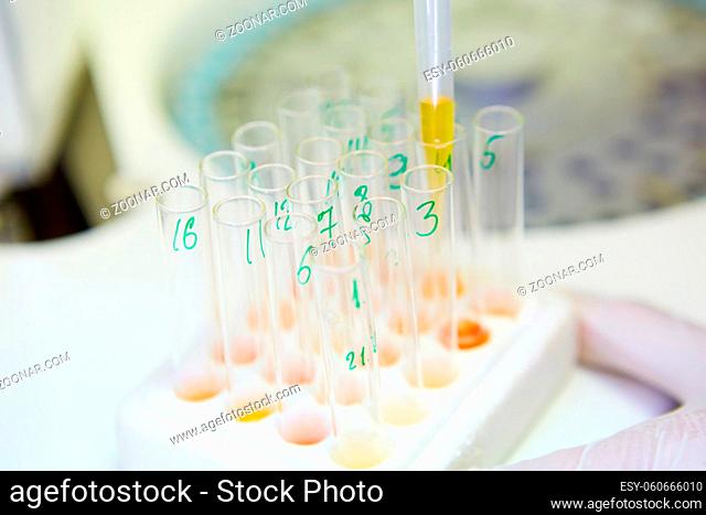 A pipette dropping sample into a test tube, abstract science background. Shallow dof