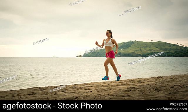 Fit young woman with a healthy lifestyle smiling while running on the beach during summer vacation in a cloudy day in Flores Island