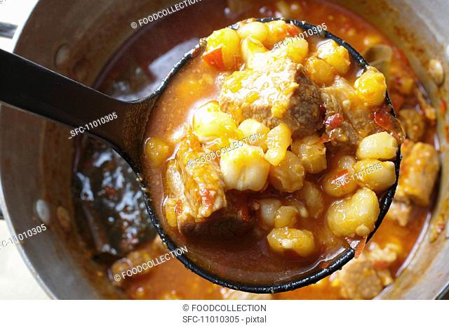 Red Posole, Mexican Hominy Stew, Made with Pork, In Ladle Above Pot