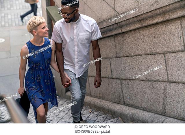 Young couple walking up steps, hand in hand, smiling