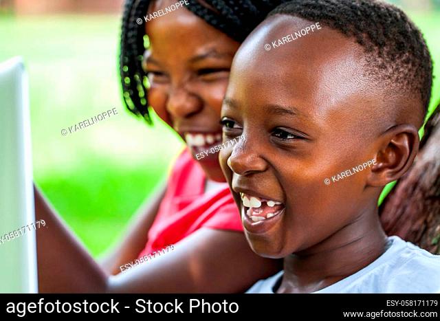 Close up face shot of African kids laughing at movie scene on digital tablet outdoors
