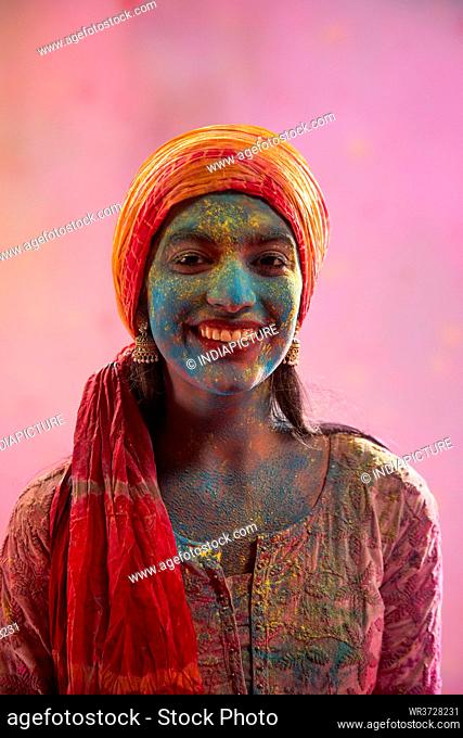 A YOUNG WOMAN WEARING PAGDI WITH HOLI COLOURS ALL OVER HER SMILING