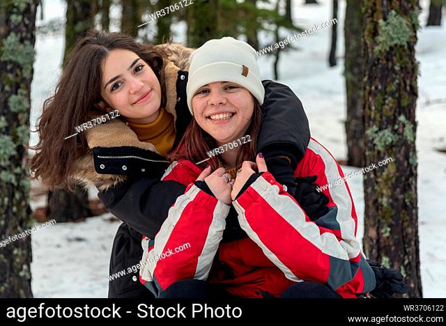 Young happy and beautiful teenage girls dressed in winter clothing laughing and hugging at snow. Troodos mountains, Cyprus