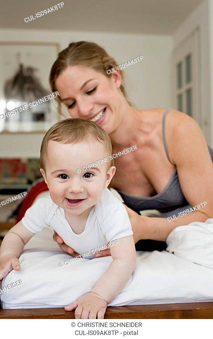 Mother guiding baby boy crawling on bed