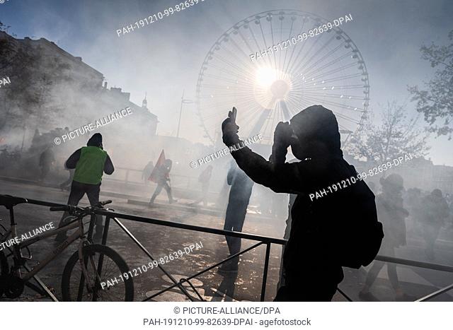 10 December 2019, France (France), Lyon: A demonstrator films himself in the haze of tear gas and pyrotechnics during a demonstration in the context of strikes...
