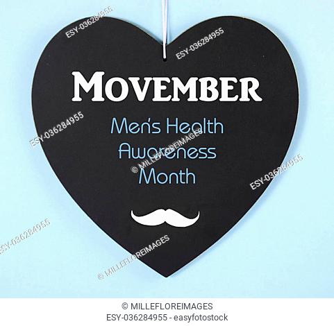 Movember fundraising for mens health awareness charity message on black heart shape blackboard on blue background