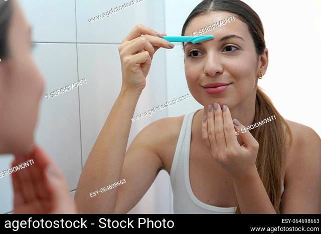Close-up of beautiful young woman shaving her face by razor at home. Pretty woman using razor on bathroom