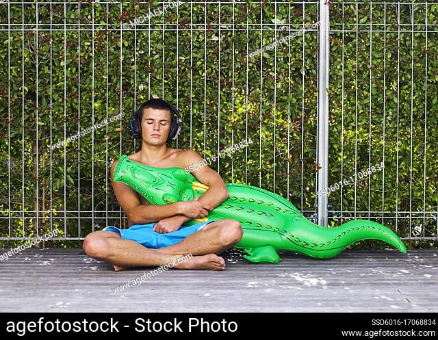 horizontal, young, man, male, youth, people, one, person, alone, fun, swimming pool, toy, blow up, crocodile, fence, hedge, holding, leisure, lifestyle, float