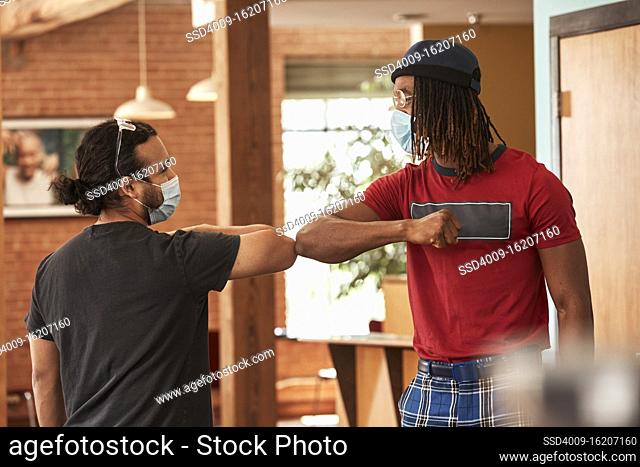 Friends in downtown loft space wearing mask, greeting each other with an elbow bump