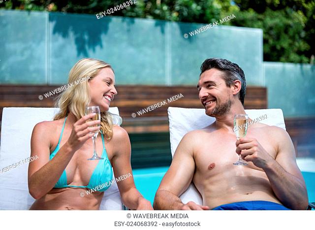 Couple sitting on sun lounger having champagne