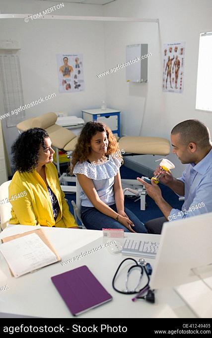 Male doctor explaining inhaler to mother and daughter in doctors office
