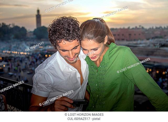 Couple in front of Jemaa el-Fnaa Square looking at smartphone, Marrakesh, Morocco