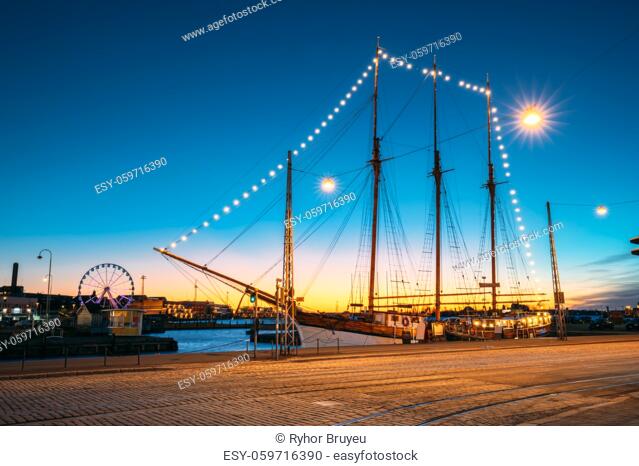 Helsinki, Finland Old Wooden Sailing Vessel Ship Schooner Is Moored To The City Pier, Jetty. Unusual Cafe Restaurant In City Center In Lighting At Evening Or...