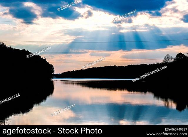 Scenic View Of Calm Lake At Sunset. River weather sun rays. Clouds. Mirror effect. Nature background