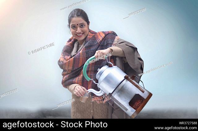 Woman with a kettle attached to an angeethi serving tea