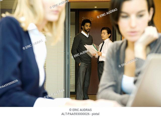 Executives discussing document in office doorway