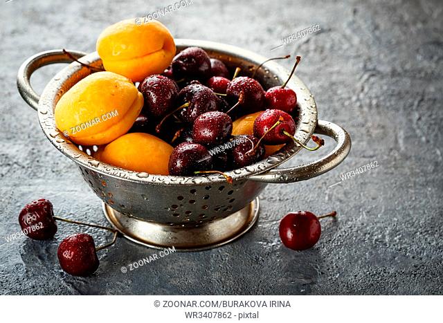 Fresh sweet cherries and apricots in metal colander