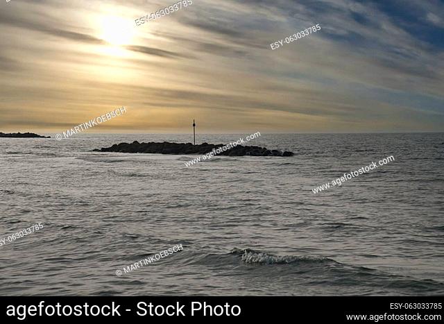 Stone groynes, breakwaters in the water off the coast in Denmark. In the evening with clouds in the sky. Landscape photo by the sea