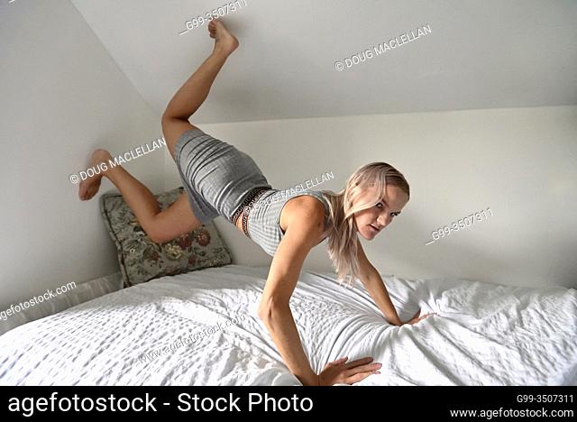 A woman in a grey dress with her feet toyching the ceiling and her hands on a bed in the autumn in Canada