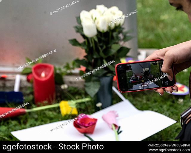 09 June 2022, Hessen, Bad Arolsen: A woman takes pictures of candles and handmade flowers in front of a stele at the secondary school Kaulbach-Schule in Bad...