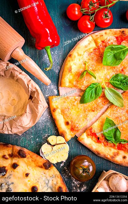 Delicious sliced pizza and ingredients for making pizza. Flour, cheese, tomatoes, basil, pepperoni, mushrooms and rolling pin over wooden background